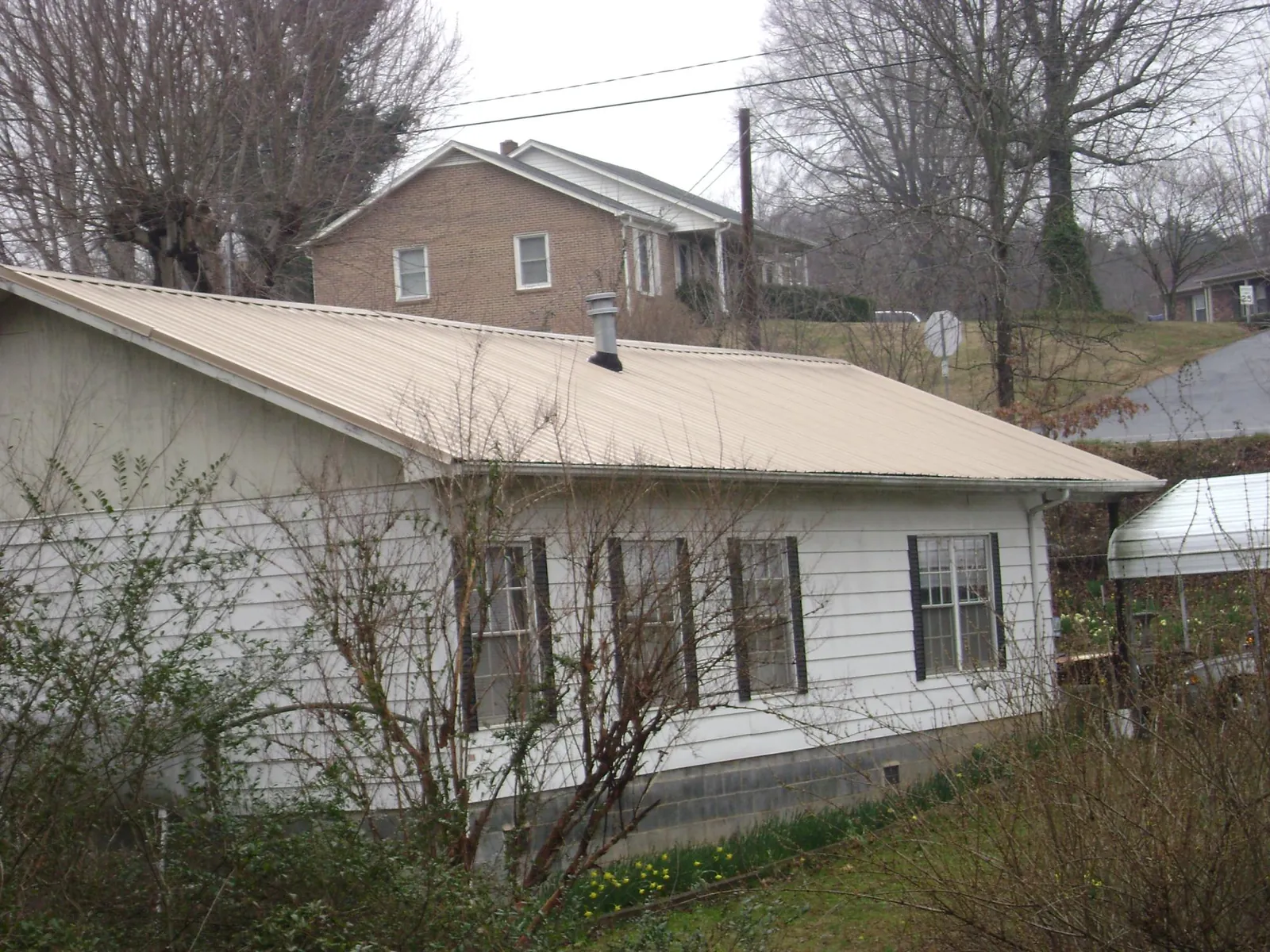 Tan metal roof on a white sided house set into a hillside — Commercial Roofing by Roofing Brothers in Crawford
