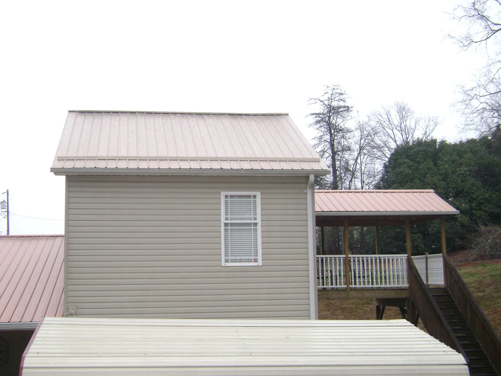 Tan metal roofs on a two story addition and attached porch, from a Roof Replacement job in Crawford